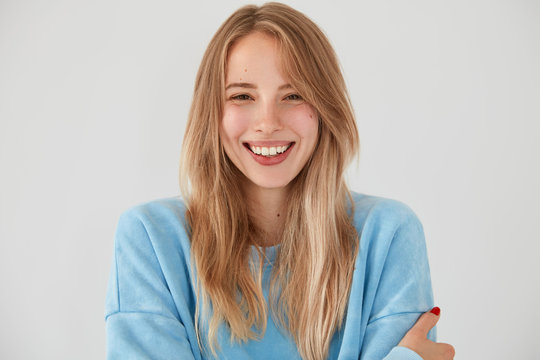 Portrait of happy attractive European female with folded arms, gentle sincere smile, being in great mood, spends spare time with boyfriend who tells funny stories, isolated over white background