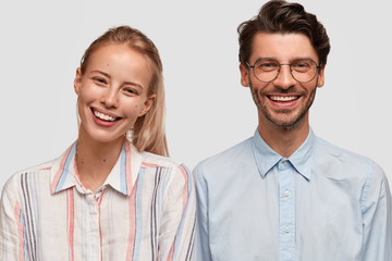 Two companions have fun, rejoice positive news, spend free time together, wear shirts, isolated over white background. Pretty female glad to meet with brother, going to have trip. Friendship concept