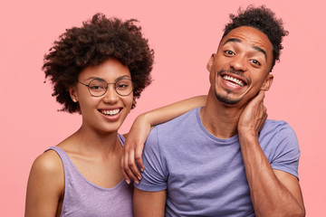 Friendly best female and male friends have positive expressions, stand closely, happy to meet after long departure, share news with each other, isolated over pink background. Cute dark skinned fellows