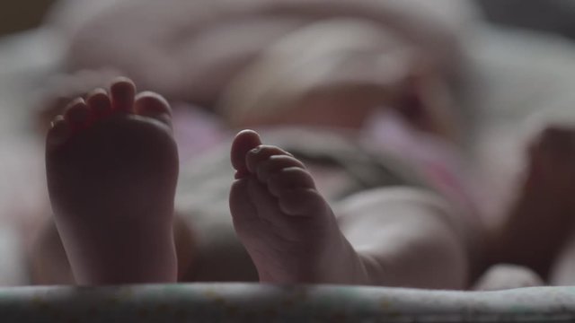 Baby lying in bouncy seat indoor, close-up shot and focus on small bare feet in foreground