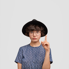 Just look upstairs! Lovely young female advertises her appartment to new host, keeps fore finger raised as shows something upwards, has serious expression, dark curly hair and healthy pure skin