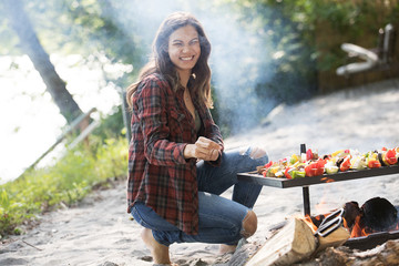Woman cooking vegetable skewers over camp fire