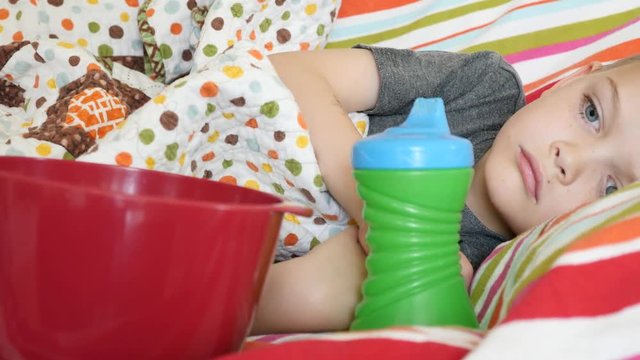 Pore little boy lies sick on the couch with a bowl