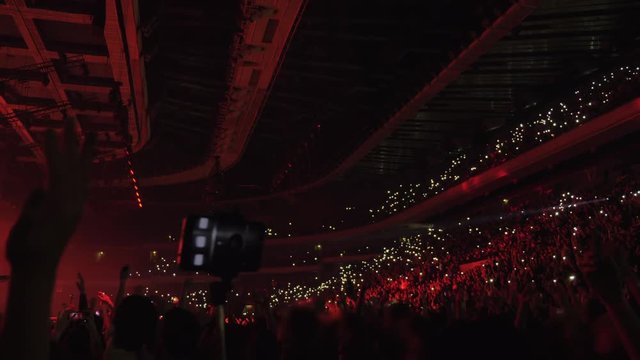 Crowded concert hall with excited people dancing and waving lights to the rhymes of favourite music. Atmosphere of unity and happiness