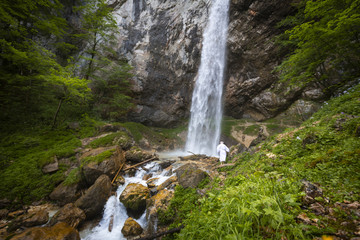 Fototapeta na wymiar European man with beard is doing waterfall-meditation while standing under big waterfall in austria, wildensteiner waterfall
