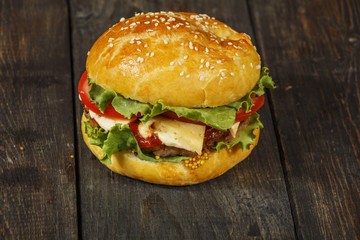 Hamburger on a wooden board against a dark background with copy space. Hamburger with sauce and fresh vegetables on a wooden table. Burger.