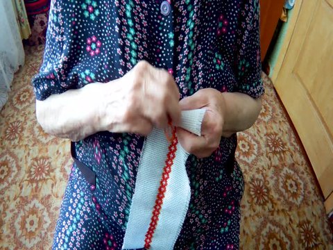 An elderly woman embroider patterns with red thread on a white cloth