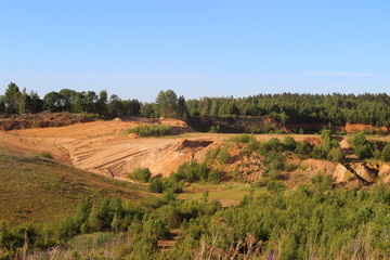 Fototapeta na wymiar Overgrown with trees and grass abandoned sand quarry in the summer in good weather against the blue clear sky