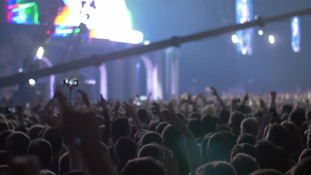 Slow motion shot of fans crowd with hands up and blinking stage lights at the music concert