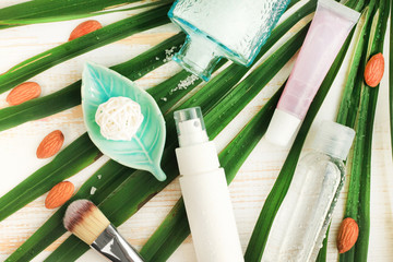 Summer skincare natural cosmetic products viewed above on fresh green palm leaf background. Facial tonic and cream, sea salt, lip balm. Home spa.