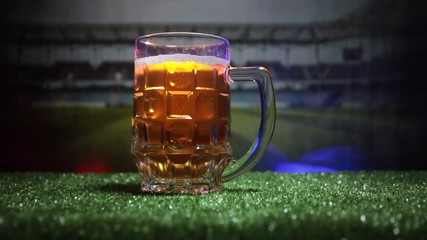 Creative concept. Pint of fresh beer on grass with blurred stadium on background with fog and light or Glass of lager beer ready for drink. Copy space. Selective focus