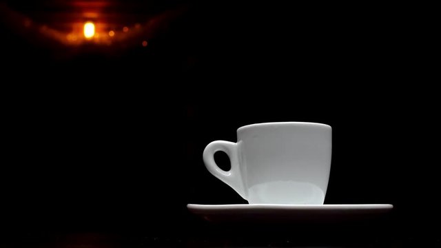 A cup of hot coffee on a black background with a lamp in the background in 4k resolution