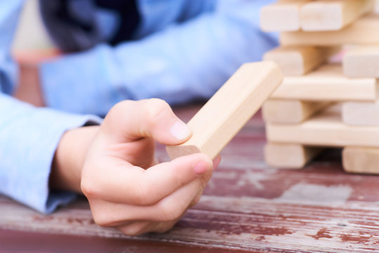 Close up kid's hand playing wood blocks tower game for practicing physical and mental skill.