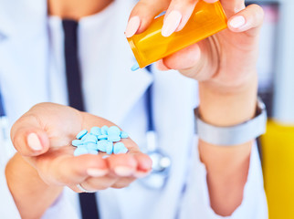 Pills are poured into female doctor hand from a jar, pills in hand, blue vitamins, orange jar with tablets, close-up.