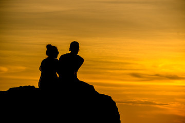 Fototapeta na wymiar Lovers are sitting on the rocks watching the sunset at the beach.