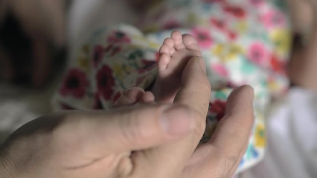 Slow motion close-up shot of grandfathers hand gently touching little feet of newborn baby