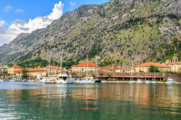 Fototapeta na wymiar Adriatic sea coastline, view to the old city Kotor surrounded by mountains and marina with yachts and boats, Mediterranean summer landscape