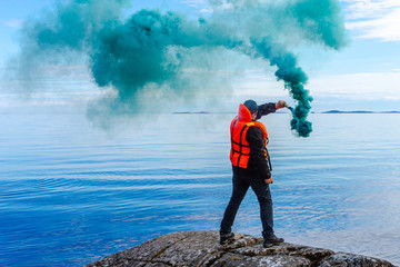 A man with a smoke torch. The rescue. Distress call. The man lights a smoke signal. A man in a life jacket. SOS