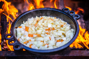 Fried vegetables on fire. Preparation of food on a fire. A rod with vegetables. Fried the onion on fire. Frying pan with fried onions and carrots.