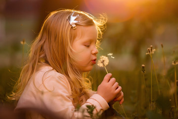 girl blowing fluffy dandelion at sunset