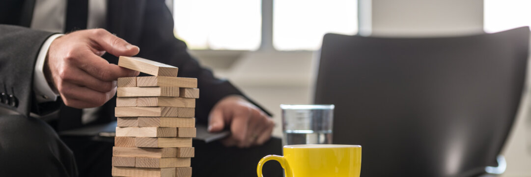 Wide panorama view of businessman in office building a tower of stacked blocks