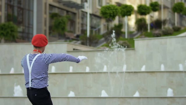 Funny mime conductor gesticulating hands at fountain background