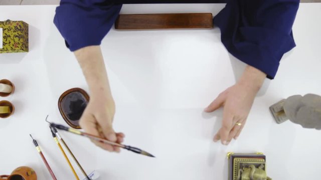 Calligraphy master draw a symbol on empty paper top view 4K. Birds eye view zoom in close up on person finished drawing calligraphy character with brush. Table of retro style contents.