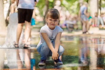 Beautiful smiling naughty little light-haired girl in jeans wearing a T-shirt walking in a sunny...