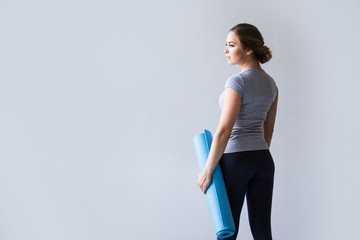 Sports woman holding yoga mat over gray.