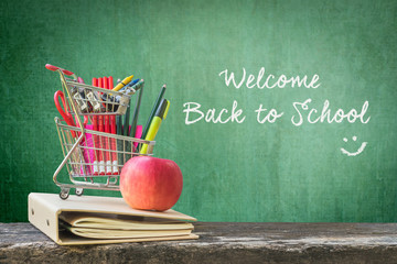 Welcome back to school happy with Shopping cart, student supplies, apple on dark old wood and green chalkboard background
