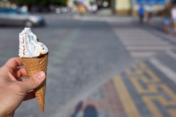 A first person view, a person walking along the road with an ice cream in his hands, shallow depth of field.