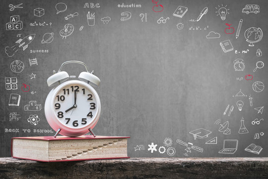 Back to school education concept with alarm clock on book on black chalkboard