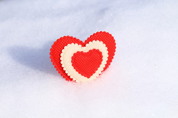 A beautiful red soft heart made of cloth in cold snow. Background. Close-up.