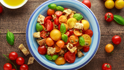 Obraz na płótnie Canvas Panzanella Tomato salad with red, yellow, orange cherry tomatoes, capers, basil and ciabatta croutons. summer healthy food.