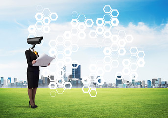 Camera headed woman standing on green grass against modern cityscape