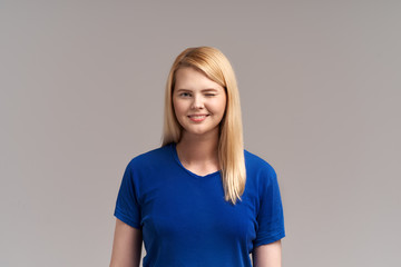 Obraz premium A pretty blonde girl smiles friendly and winks with a friendly smile. Studio horizontal portrait. The concept of positive emotions and feelings