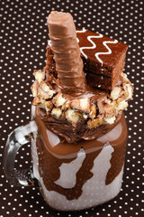 Chocolate extreme milkshake with brownie cake, chocolate paste and sweets. Crazy freakshake food trend.