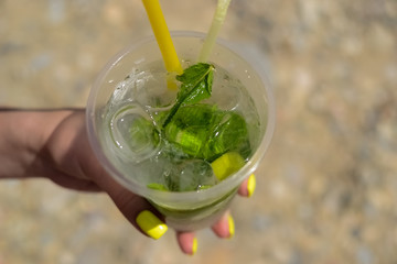 the maiden's hand holds a transparent glass of ice with lemon and mint. Mojito