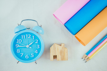 Alarm clock, pencil and color paper on table.