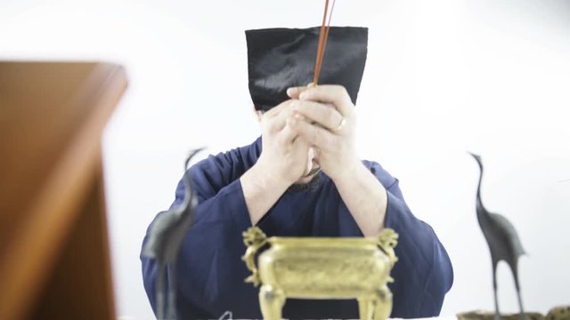 Daoist Ritual person put incense inside golden chest 4K. Low angle front view dolly slide behind ritual chest with man in background in focus holding incense. Wearing blue kimono.