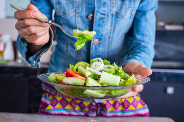 Woman hands holds, tastes vegetables salad with fork. Cucumbers, tomatoes, onion rings, unrefined sunflower oil, rock salt. Raw vegan vegetarian healthy food
