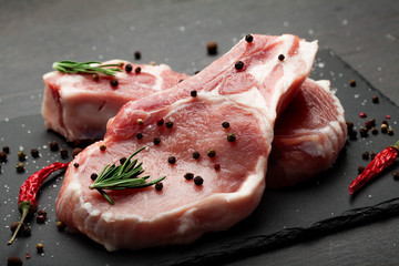 fresh raw meat with spices and rosemary and red pepper on black slate, on dark background, pork,...
