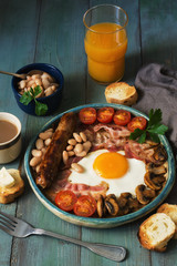 Full English breakfast with scrambled eggs, sausage, mushrooms, beans and bacon on a wooden rustic green table.Toast with butter, coffee and orange juice.