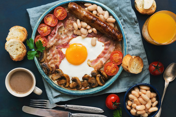 Traditional English breakfast. Fried egg with sausage, mushrooms, beans, tomatoes and bacon. View from above.Toast with butter, coffee and orange juice.