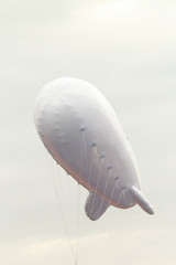 Fototapeta premium White inflatable dirigible with a place for a logo on a background of a gray sky with clouds