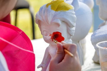 Hand of the child paints a doll in watercolor paints in an art studio