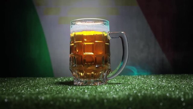 Creative concept. Pint of fresh beer on grass with blurred flag of Italy on background or Glass of lager beer ready for drink. Copy space. Selective focus