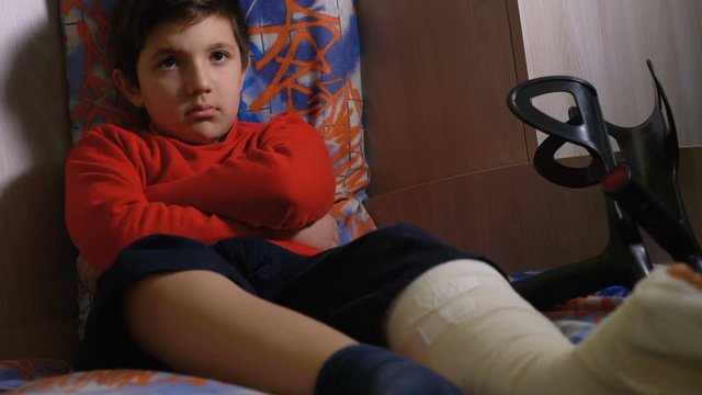 Angry sad kid with leg's plaster alone in his bedroom