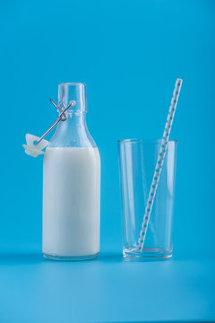 Glass bottle of fresh milk and a glass with a straw on a blue background. Concept of healthy dairy products with calcium