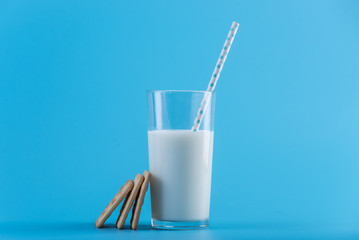 Glass of fresh cow milk with a straw and cookies on a blue background. Concept of healthy dairy products with calcium